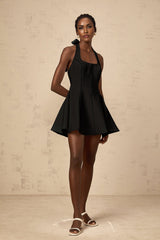 Woman wearing black halterneck mini dress with bow detail at neckline