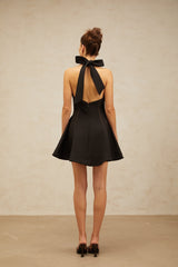 Woman wearing black halterneck mini dress with bow detail at neckline