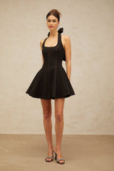 Woman wearing black halterneck mini dress with bow detail at the neck