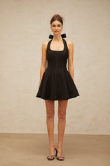 Woman wearing black halterneck mini dress with bow detail