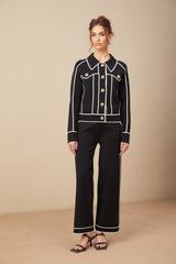 Woman wearing black jacket and trousers set with white piping detail