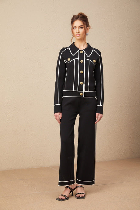 Woman wearing black jacket and trousers set with white piping detail
