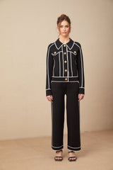 Woman wearing black jacket and trousers set with white piping detail