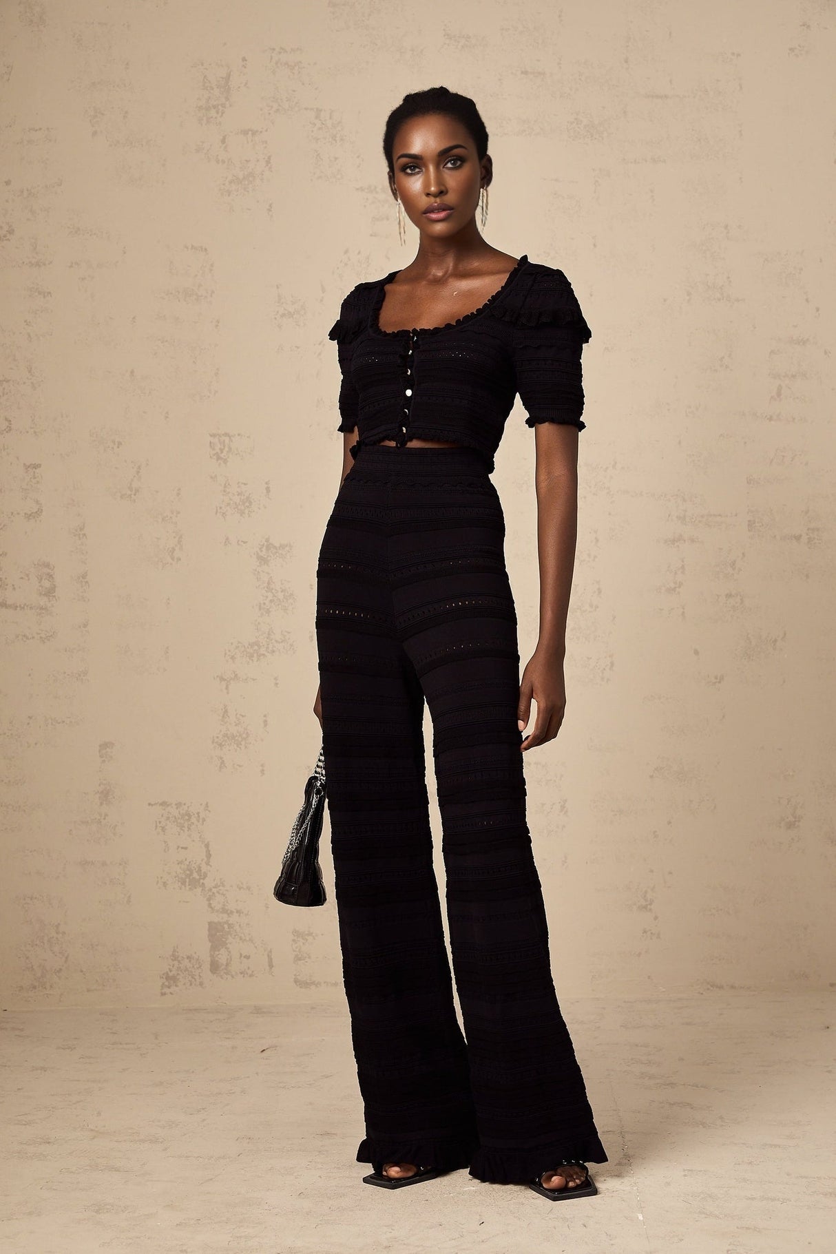 Woman wearing black knitted matching set with ruffled top and trousers