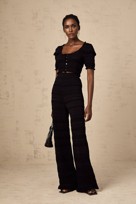 Woman wearing black knitted matching set with ruffled top and trousers