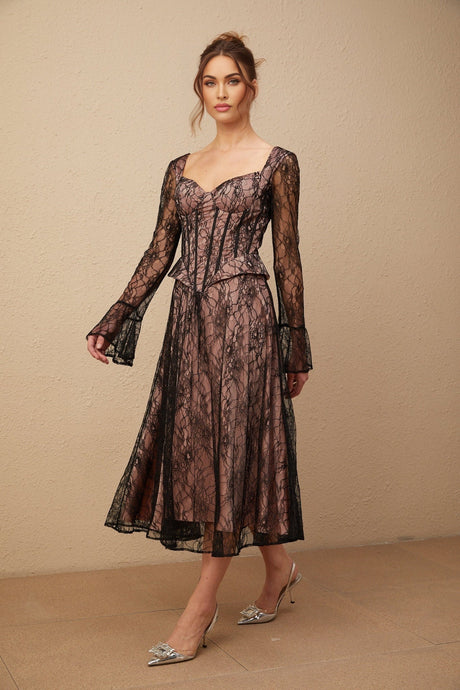 Woman wearing black lace midi dress with flared skirt and fitted bodice standing against plain background