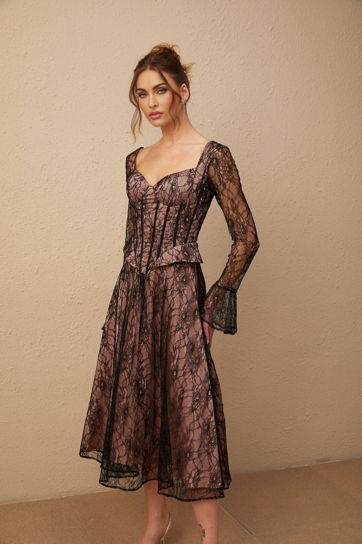 Woman wearing black lace midi dress with flared skirt and fitted bodice standing against plain background