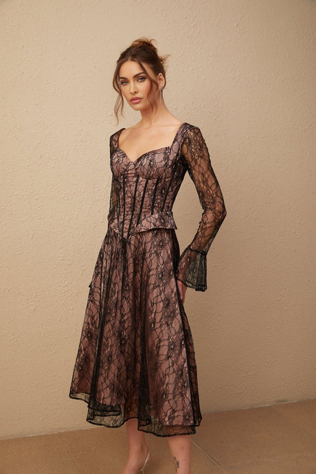 Woman wearing black lace midi dress with flared skirt and fitted bodice standing against plain background