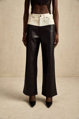 Woman wearing black leather trousers with contrasting white side panels and pockets standing against plain background