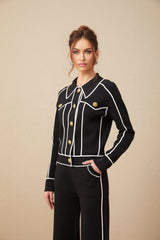 Woman wearing black matching jacket and trousers set with white piped trim detail