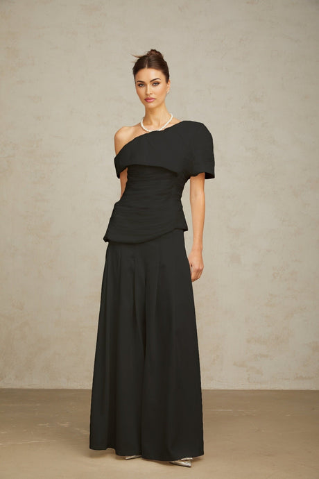 Woman wearing black matching set with creased top and trousers standing against plain background