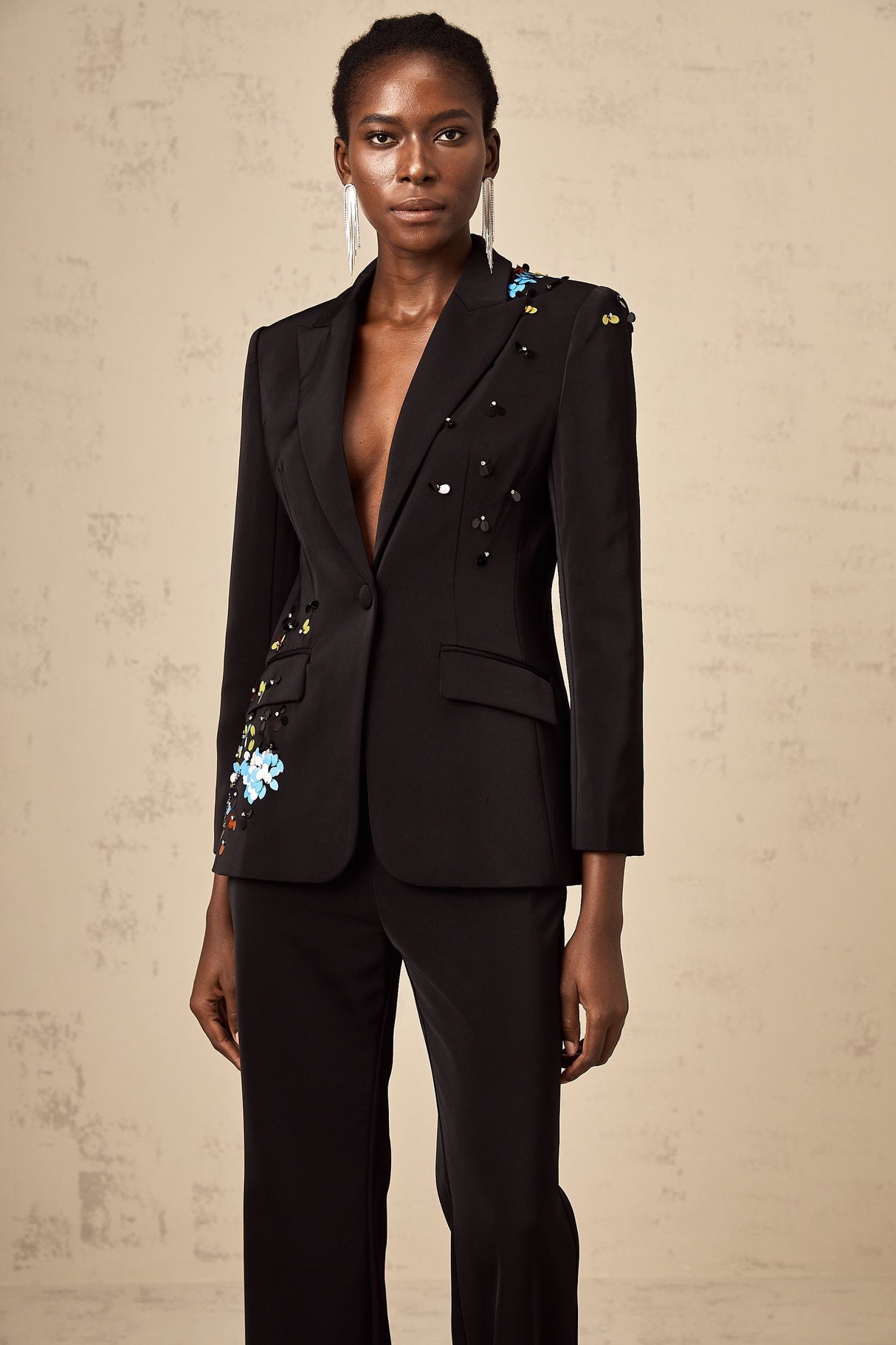 Woman wearing black sequined blazer and matching trousers standing against plain background