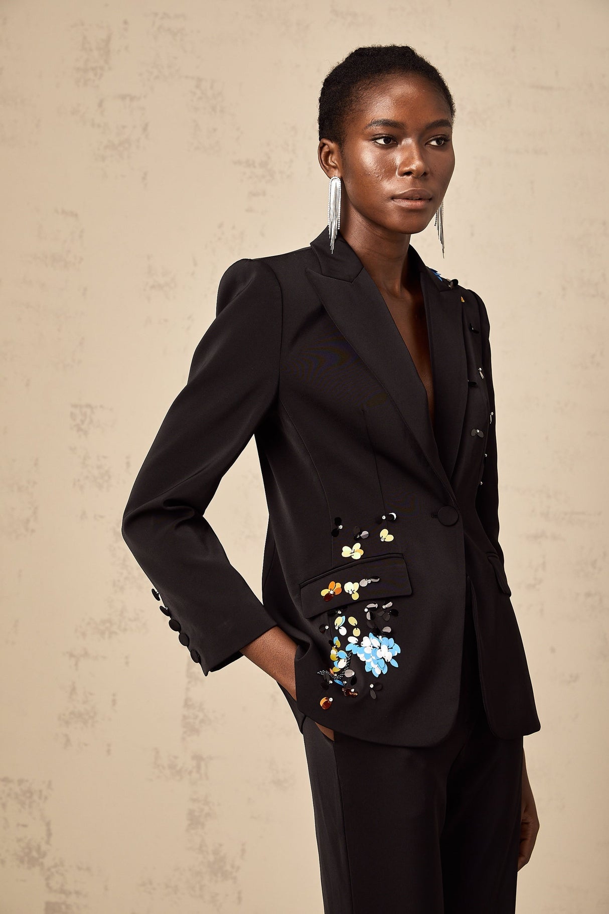 Woman wearing black sequined blazer and matching trousers standing against plain background
