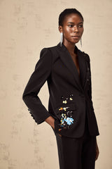 Woman wearing black sequined blazer and matching trousers standing against plain background