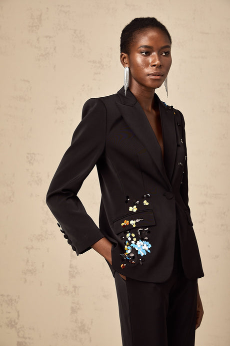 Woman wearing black sequined blazer and matching trousers standing against plain background