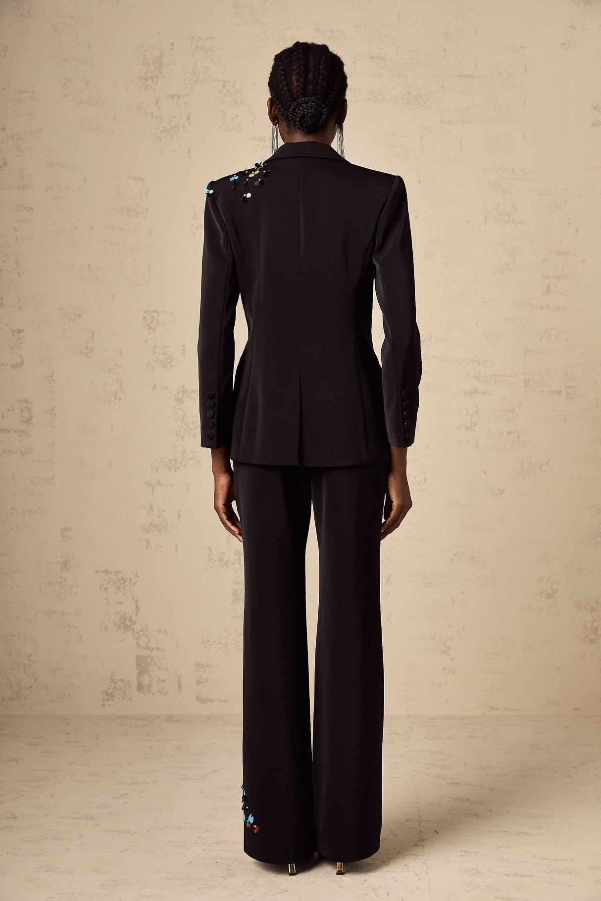 Woman wearing black sequined blazer and matching trousers standing against plain background