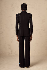 Woman wearing black sequined blazer and matching trousers standing against plain background