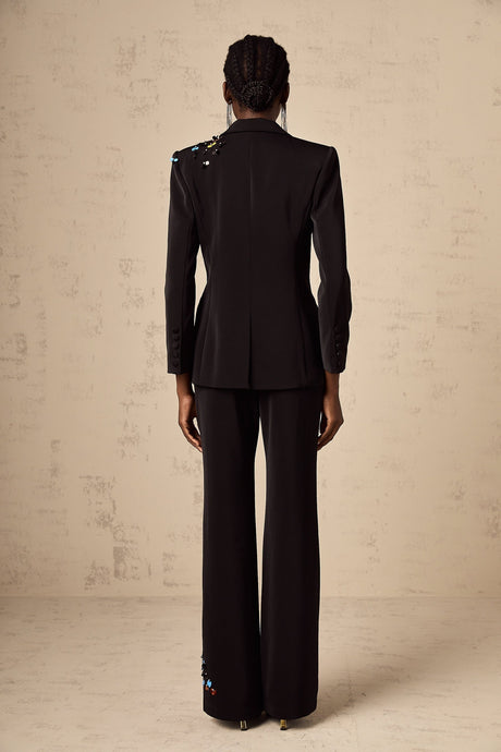 Woman wearing black sequined blazer and matching trousers standing against plain background