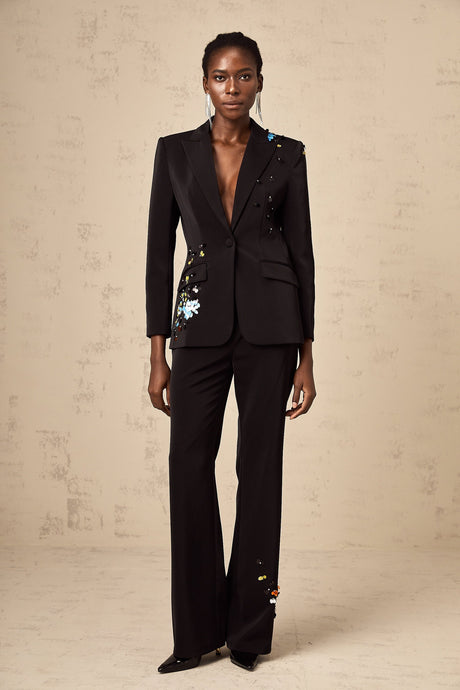 Woman wearing black sequined blazer and matching trousers standing against plain background