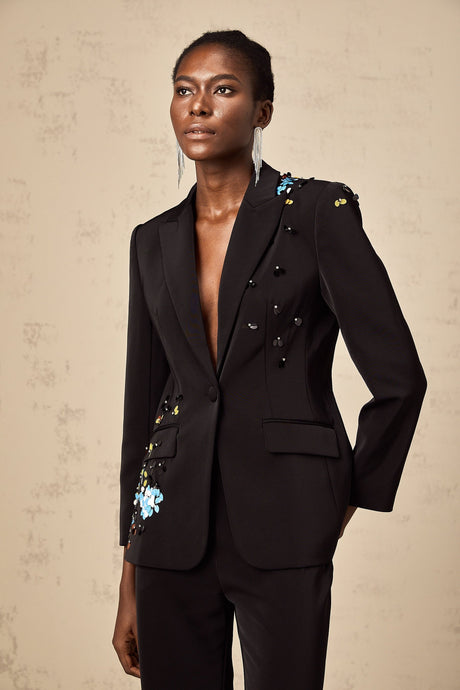 Woman wearing black sequined blazer and matching trousers standing in formal pose