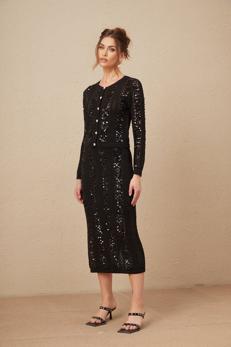Woman wearing black sequined cardigan and matching skirt set with crochet knit pattern