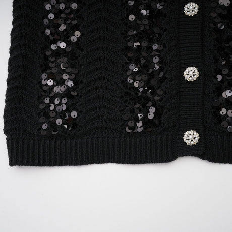 Woman wearing black sequined crochet knit cardigan and matching skirt set against plain background