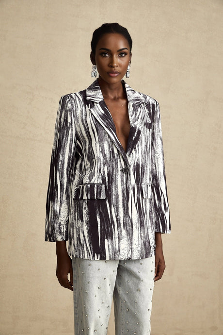 Woman wearing black textured jacket with graffiti print design standing against plain background