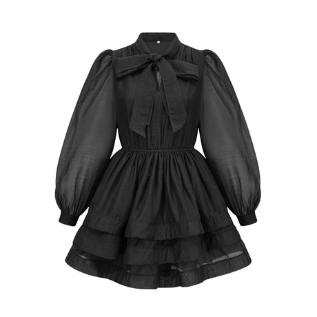 Woman wearing black tiered flared mini dress with short sleeves and round neckline standing against plain background