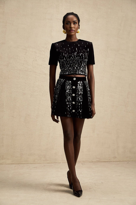 Woman wearing black velvet two piece outfit with embellished top and matching skirt