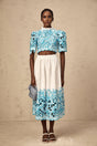 Woman wearing blue embroidered crop top and matching skirt with cutout details standing against light background