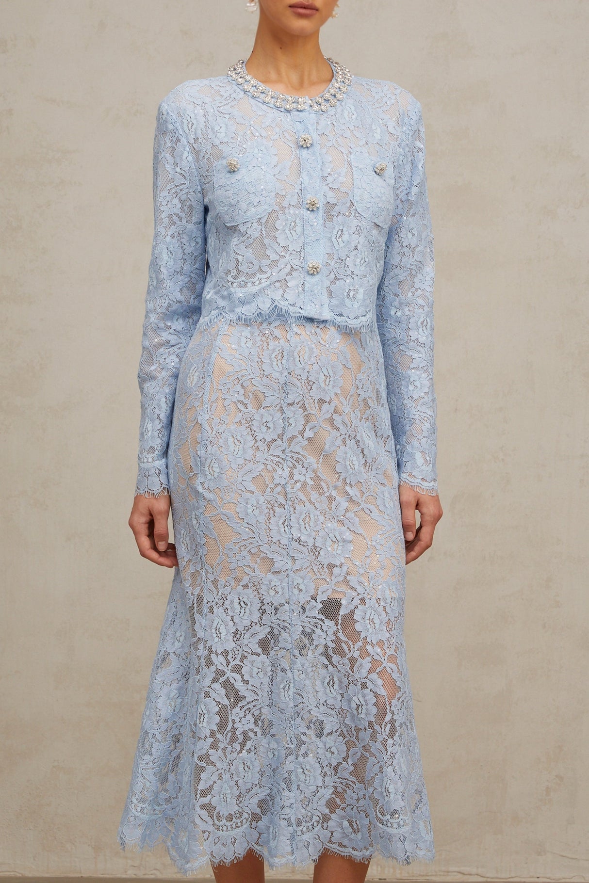 Woman wearing blue floral lace crop top and matching skirt set against plain background
