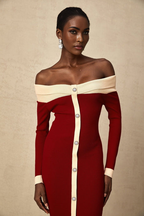 Woman wearing blue offshoulder knit midi dress with fitted silhouette standing against plain background