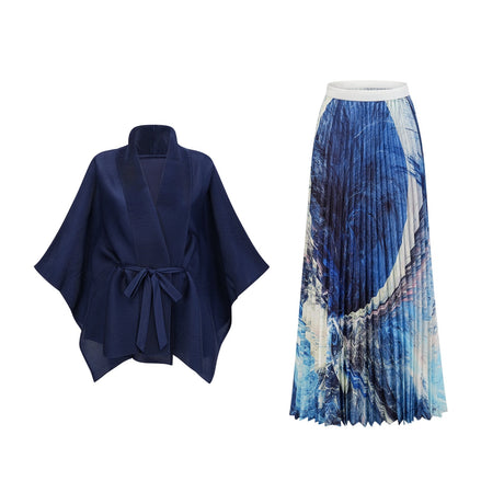 Woman wearing blue patterned cape and matching skirt set with creased texture standing against plain background
