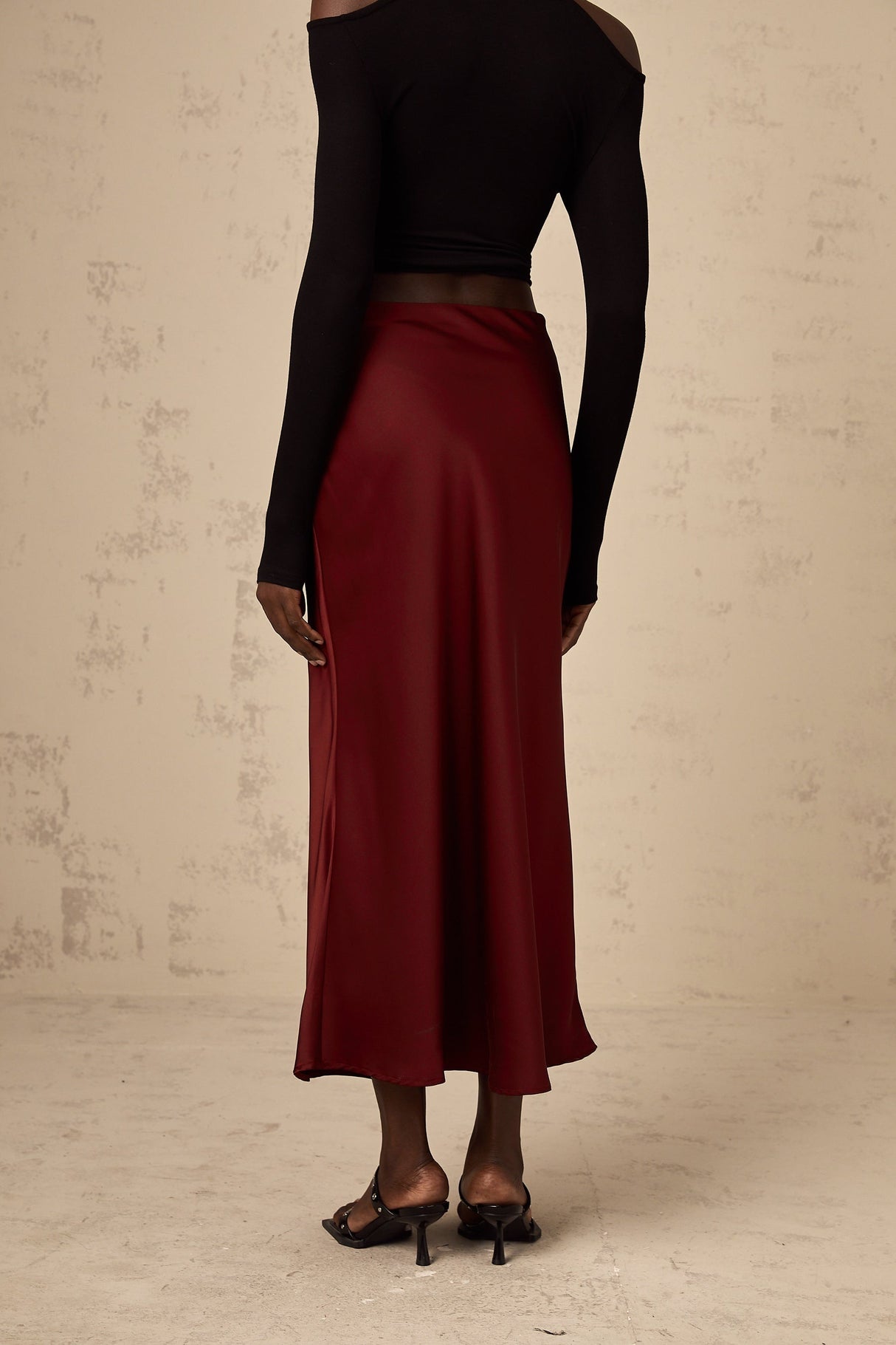 Woman wearing bright red satin skirt with flared silhouette against plain background