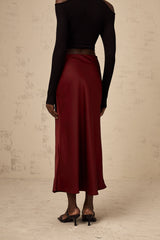 Woman wearing bright red satin skirt with flared silhouette against plain background