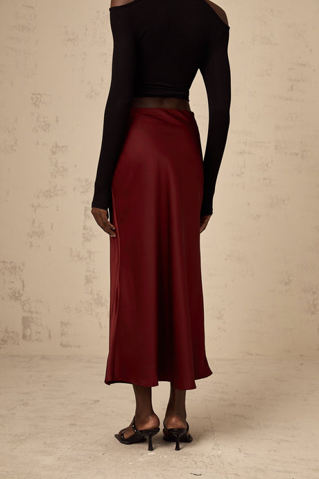 Woman wearing bright red satin skirt with flared silhouette against plain background