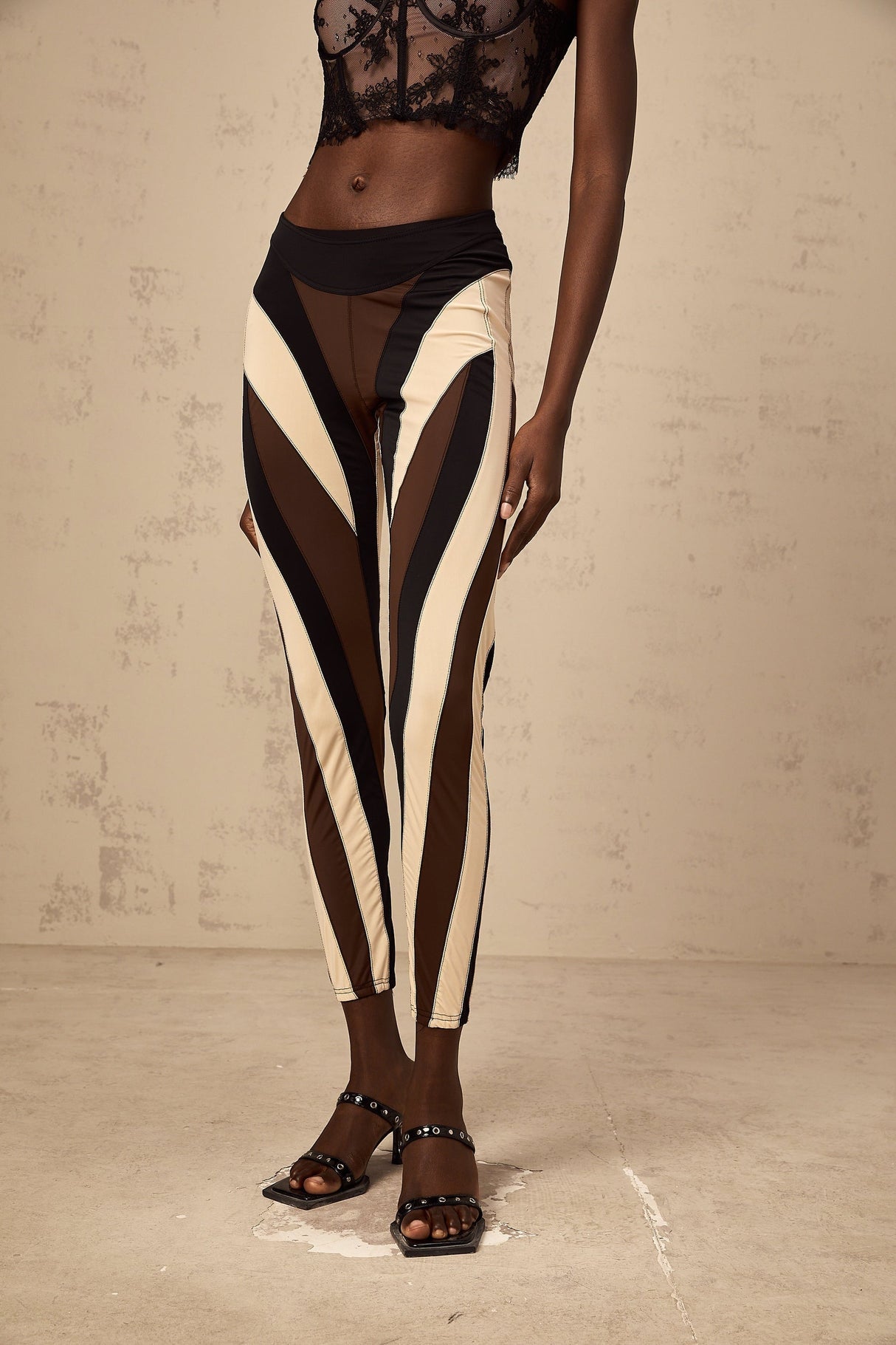 Woman wearing colorful spiral patterned leggings with color block panels in various shades standing against plain background