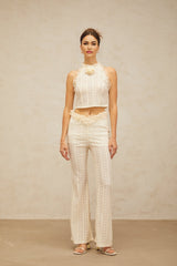 Woman wearing cream white jacquard matching set with ruffled lace trim top and trousers standing against plain background