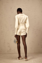 Woman wearing crystal embellished jacket and matching shorts set in light color standing against plain background