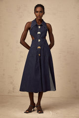 Woman wearing dark blue denim midi dress with cut out details on sides standing against plain background