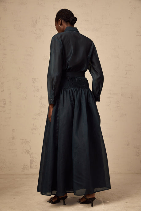 Woman wearing dark green matching set with ribbon tie neck shirt and skirt
