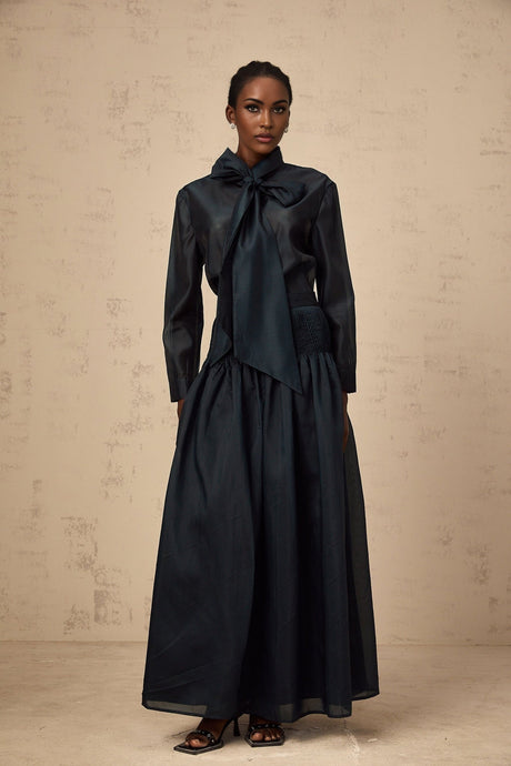 Woman wearing dark green matching set with ribbon tie neck shirt and skirt