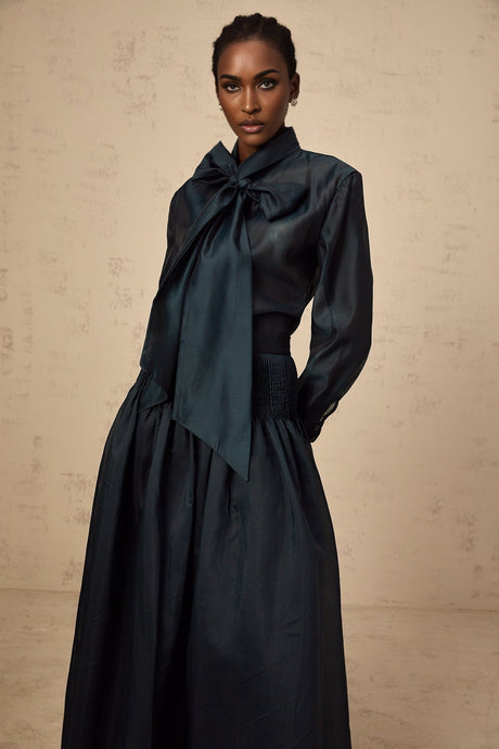 Woman wearing dark green matching set with ribbon tieneck shirt and coordinating skirt