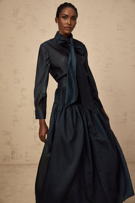 Woman wearing dark green matching set with shirt and skirt Shirt has ribbon tie neck detail