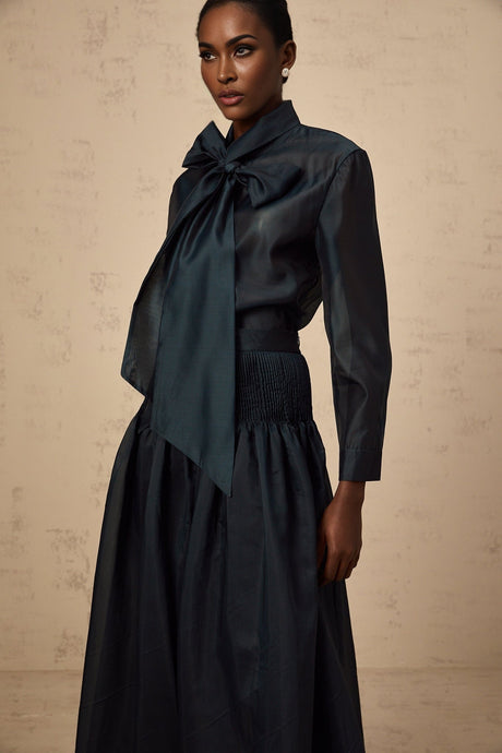 Woman wearing dark green matching set with tieneck shirt and skirt ribbon detail