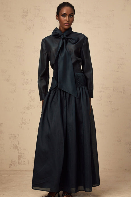 Woman wearing dark green matching shirt and skirt set with ribbon tie at neck