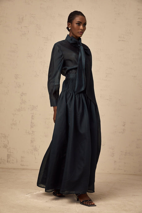 Woman wearing dark green matching shirt and skirt set with ribbon tie neck detail