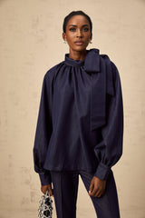Woman wearing denim blue flared blouse and matching trousers standing against plain background