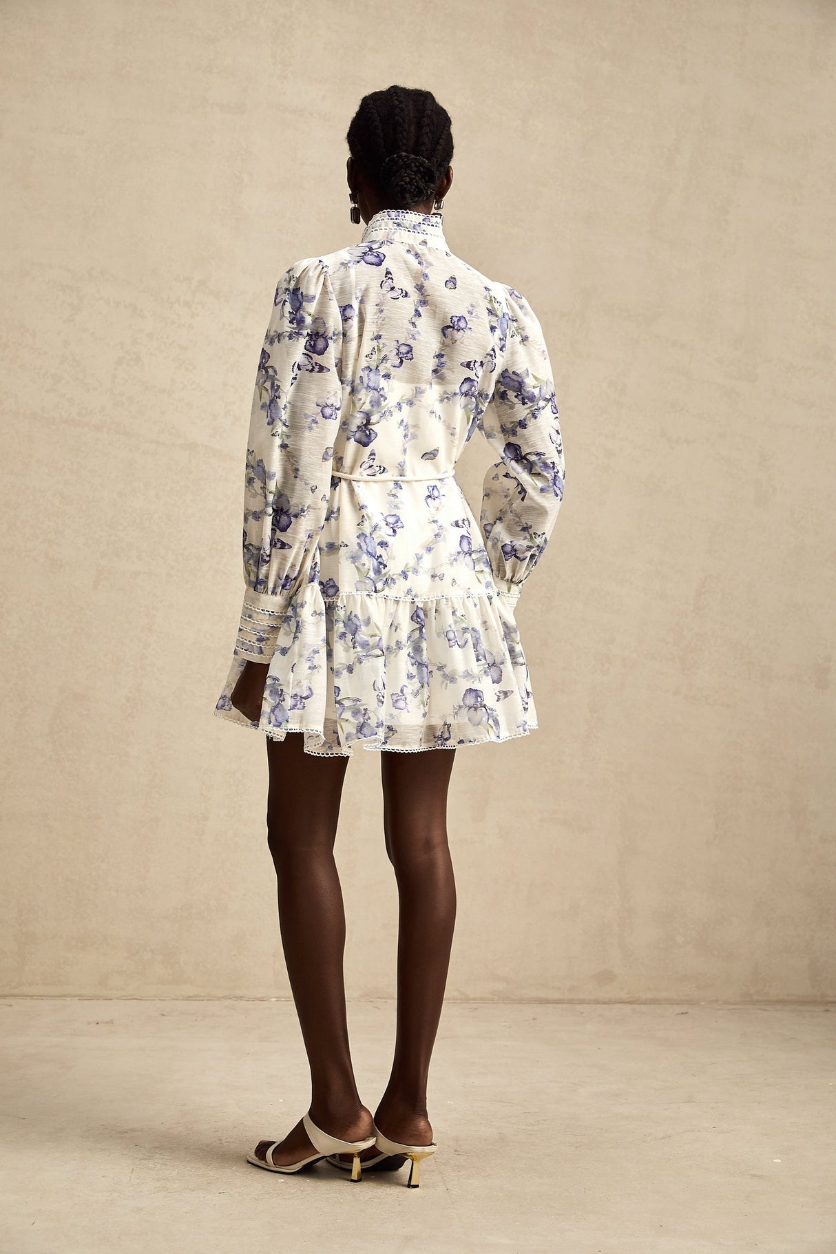 Woman wearing floral print chiffon mini dress with flared skirt and short sleeves standing against plain background
