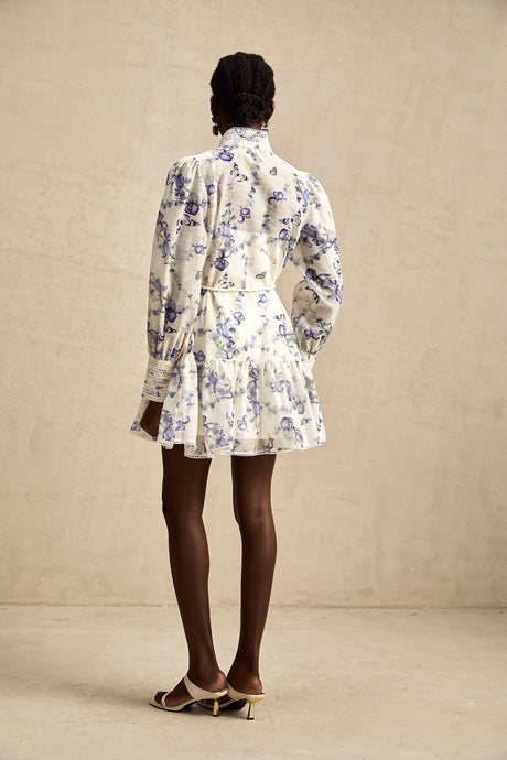 Woman wearing floral print chiffon mini dress with flared skirt and short sleeves standing against plain background